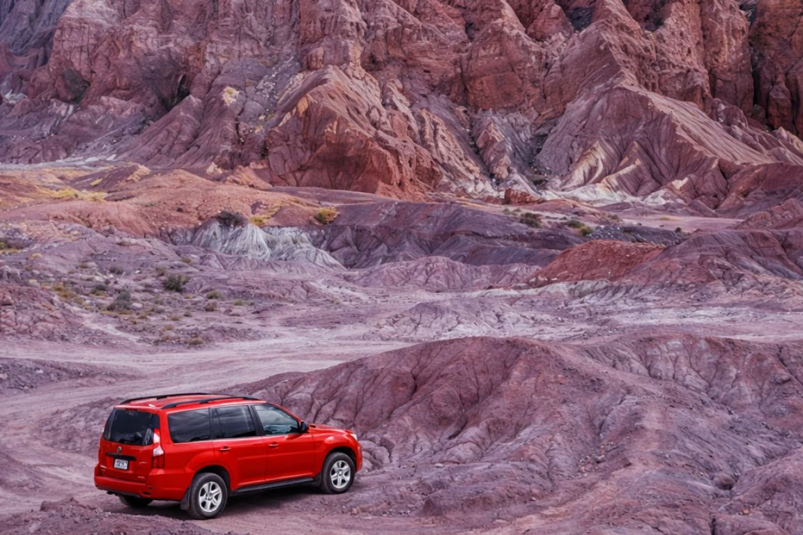 Exploring the Atacama Desert by car on a guided tour with Atacama Chile Tours, featuring a red SUV among layered volcanic rock formations