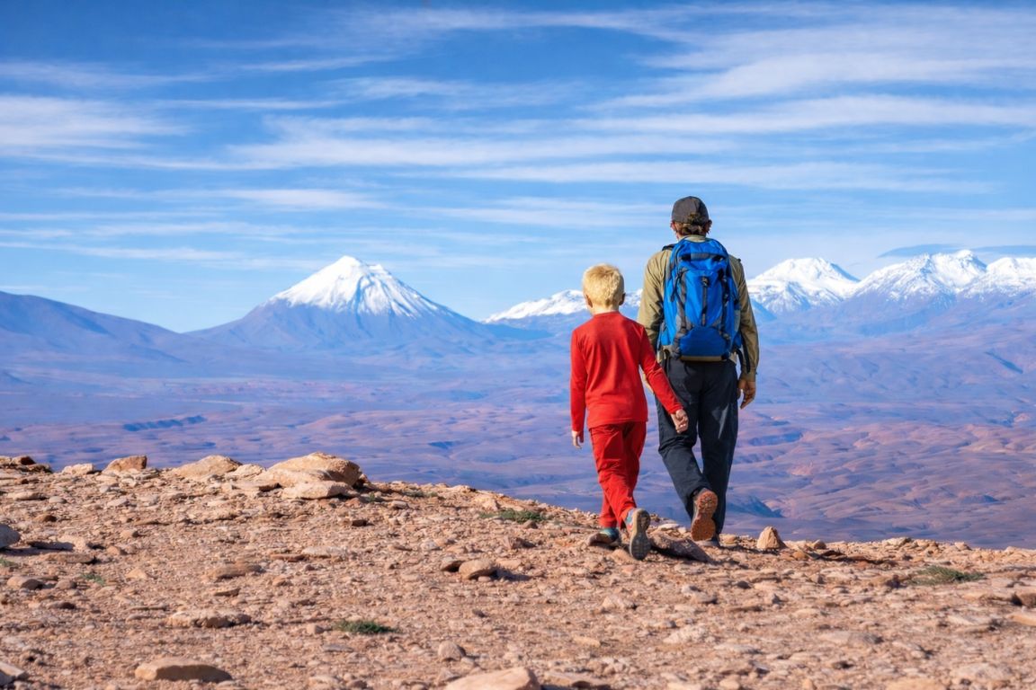 Adult and child hiking together through the Atacama Desert with volcanoes in the background during a private family tour with Atacama Chile Tours.