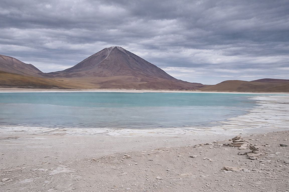 Salar de Uyuni salt flats with turquoise lagoon and volcano under cloudy skies, photographed during a guided tour with Atacama Chile Tours